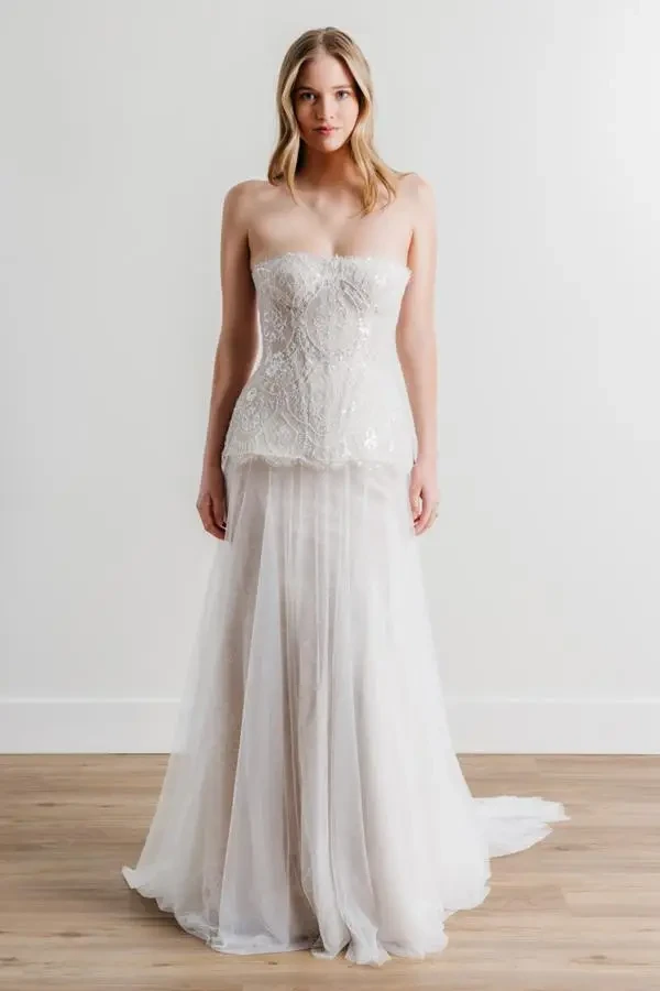 Model wears a strapless A-line gown with beaded lace, sparkle accents, and a panier-style overskirt.