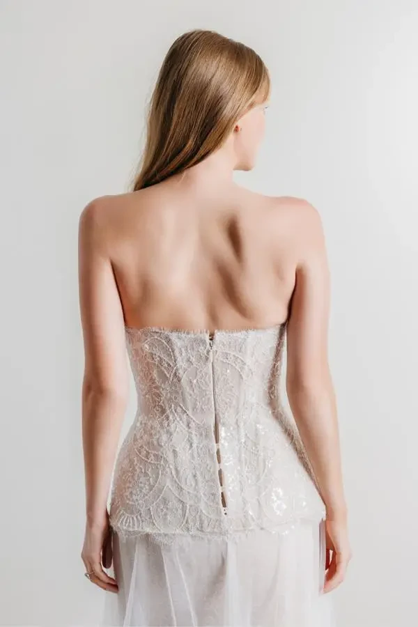Model wears a strapless A-line gown with beaded lace, sparkle accents, and a panier-style overskirt.