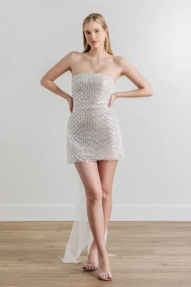 Model is wearing a sparkling beaded mini dress with an inner corset, knit lining, and a detachable tulle bow