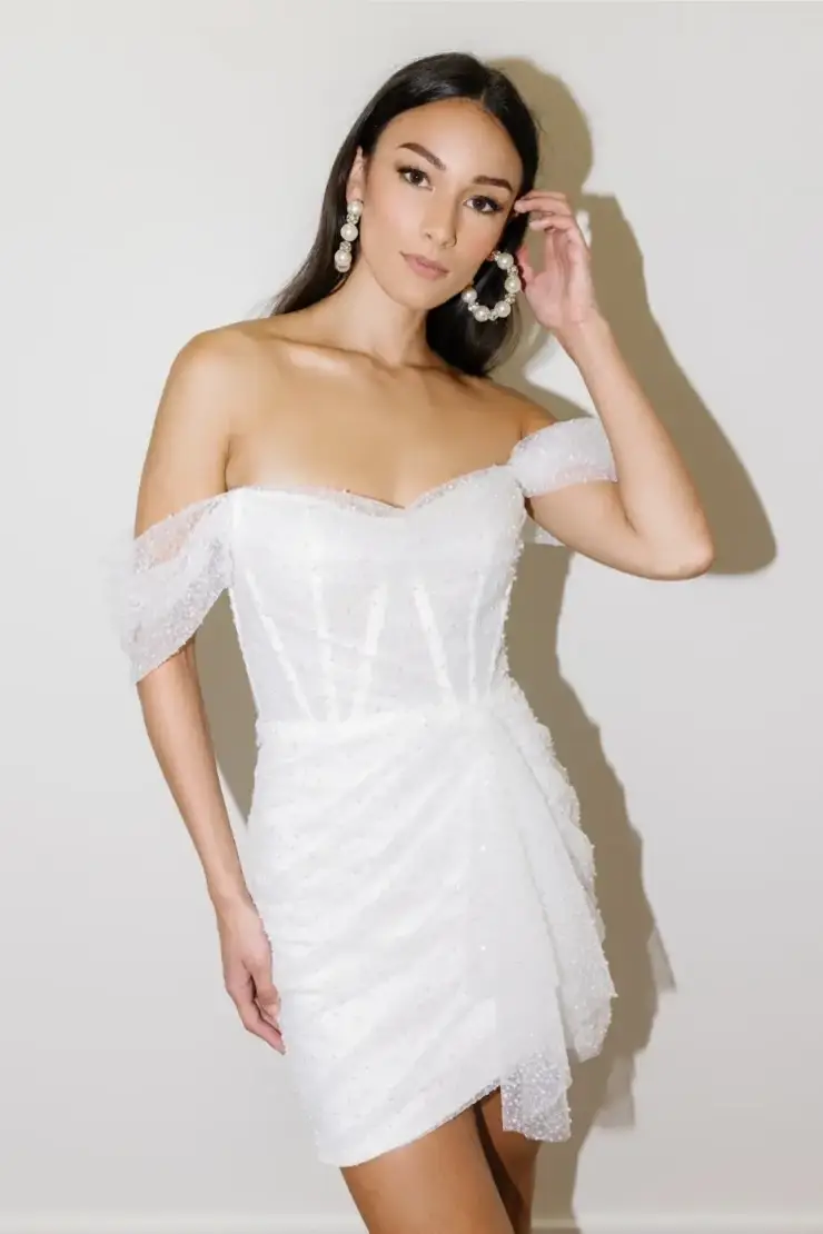 Model is wearing a mini wedding dress with all-over beading and a structured corseted bodice