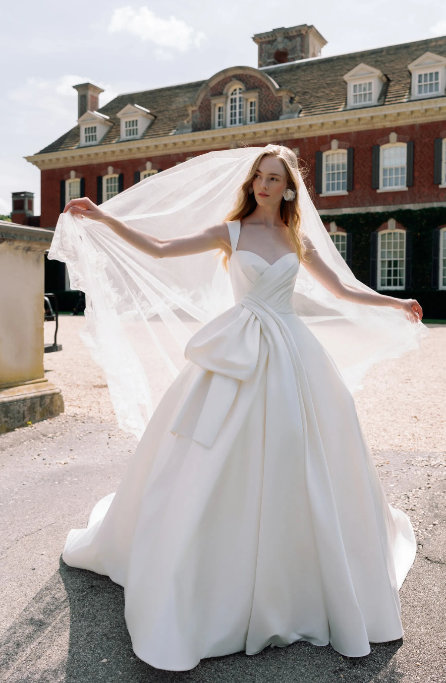 A bride wearing a white wedding gown, holding a veil outdoors.