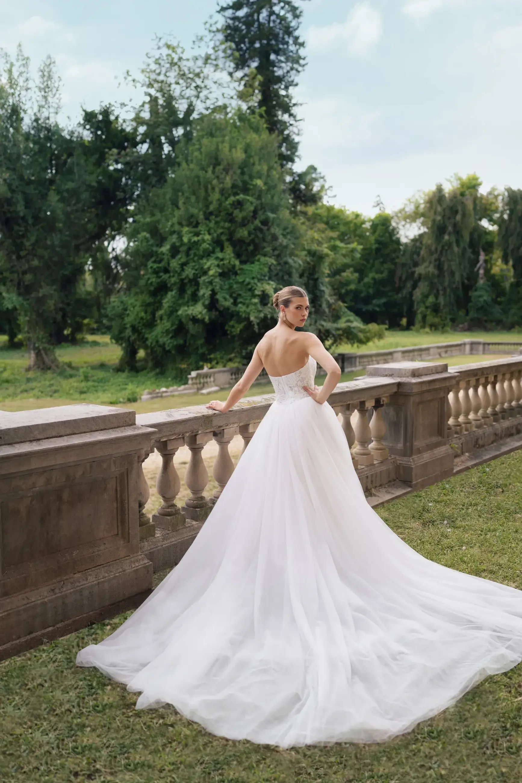 Model wears a strapless lace bodice gown with a pleated tulle skirt, basque waist, and long train.