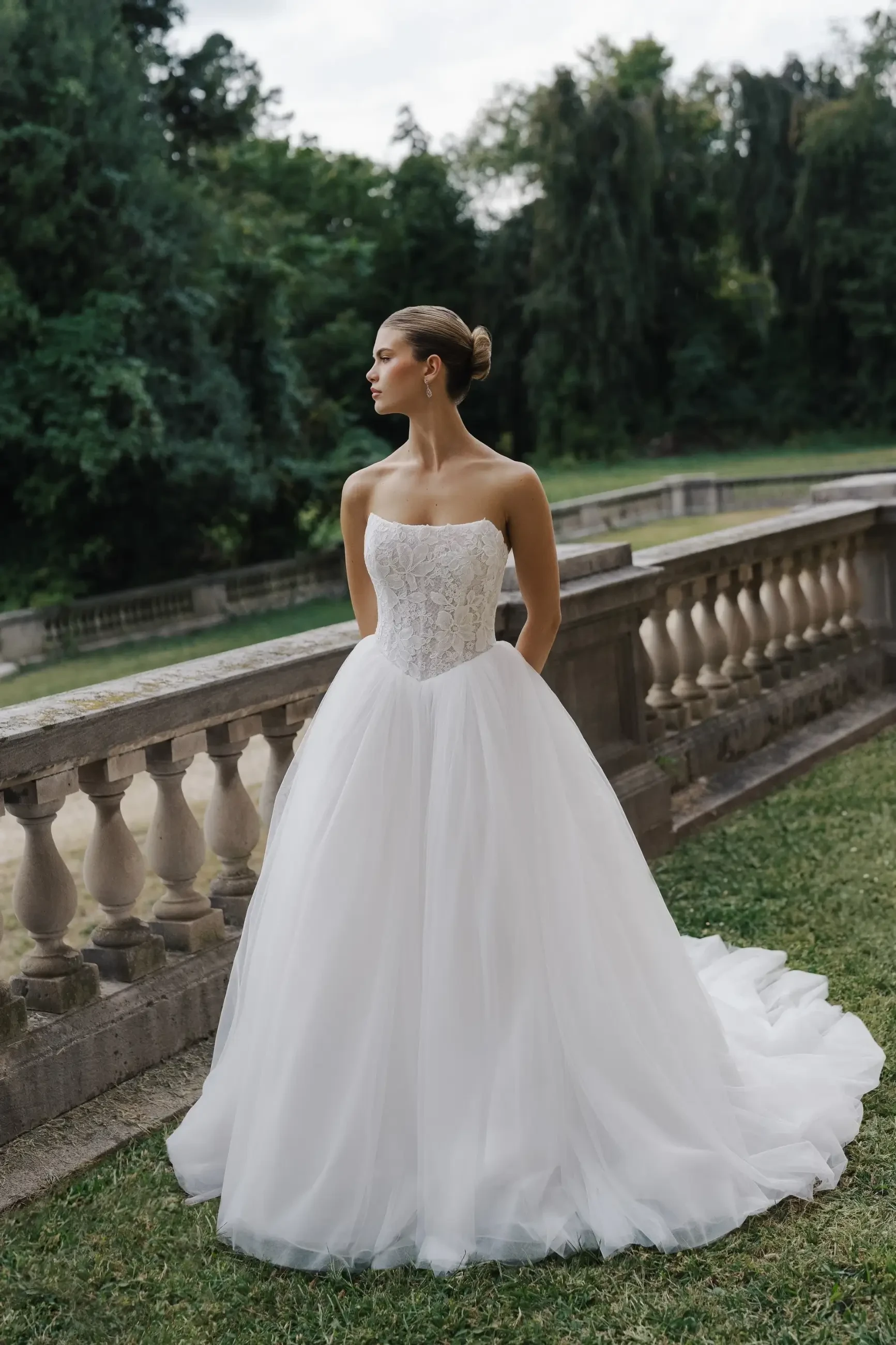 Model wears a strapless lace bodice gown with a pleated tulle skirt, basque waist, and long train.