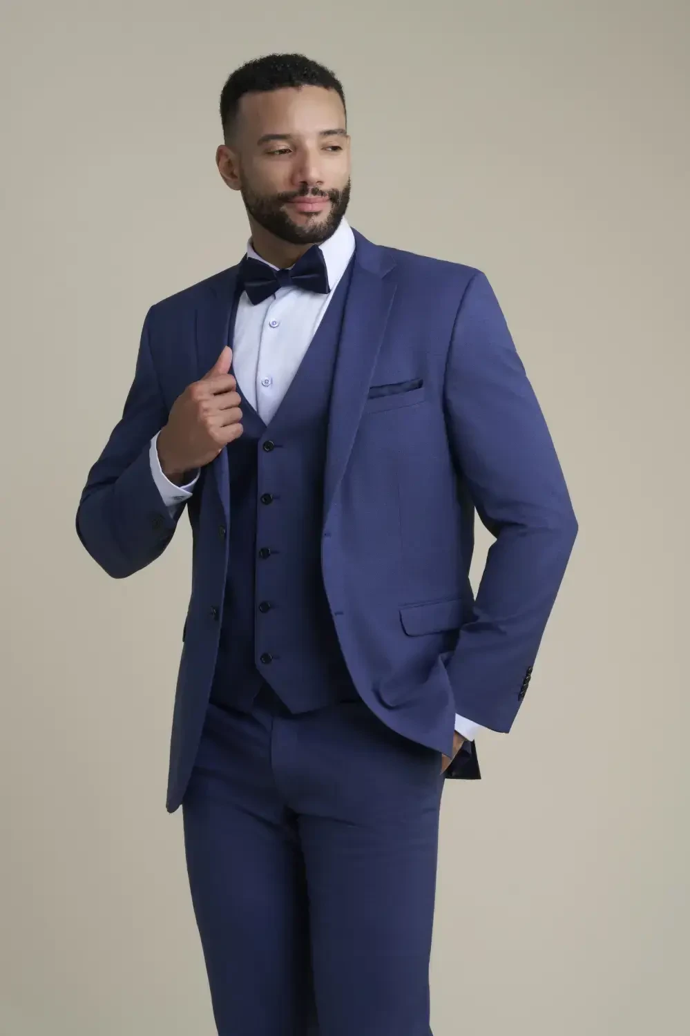 A man in a stylish navy blue suit and bow tie, looking confidently to the side against a neutral background.
