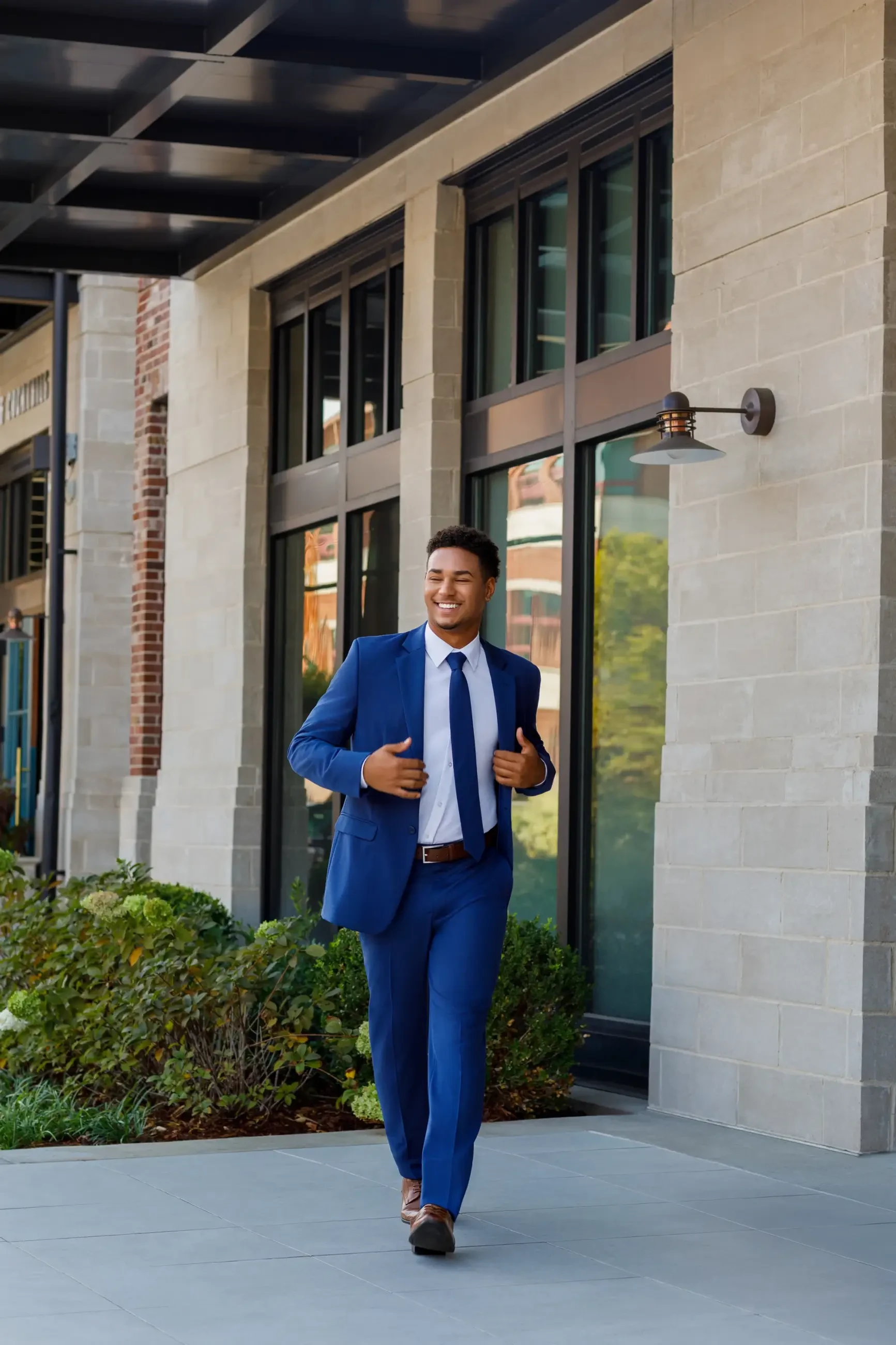 A man in a blue suit and tie walking confidently outside a modern building with large windows.